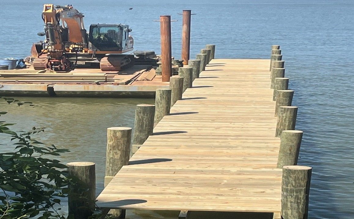 A newly constructed wooden dock extending over the water with construction equipment on a barge