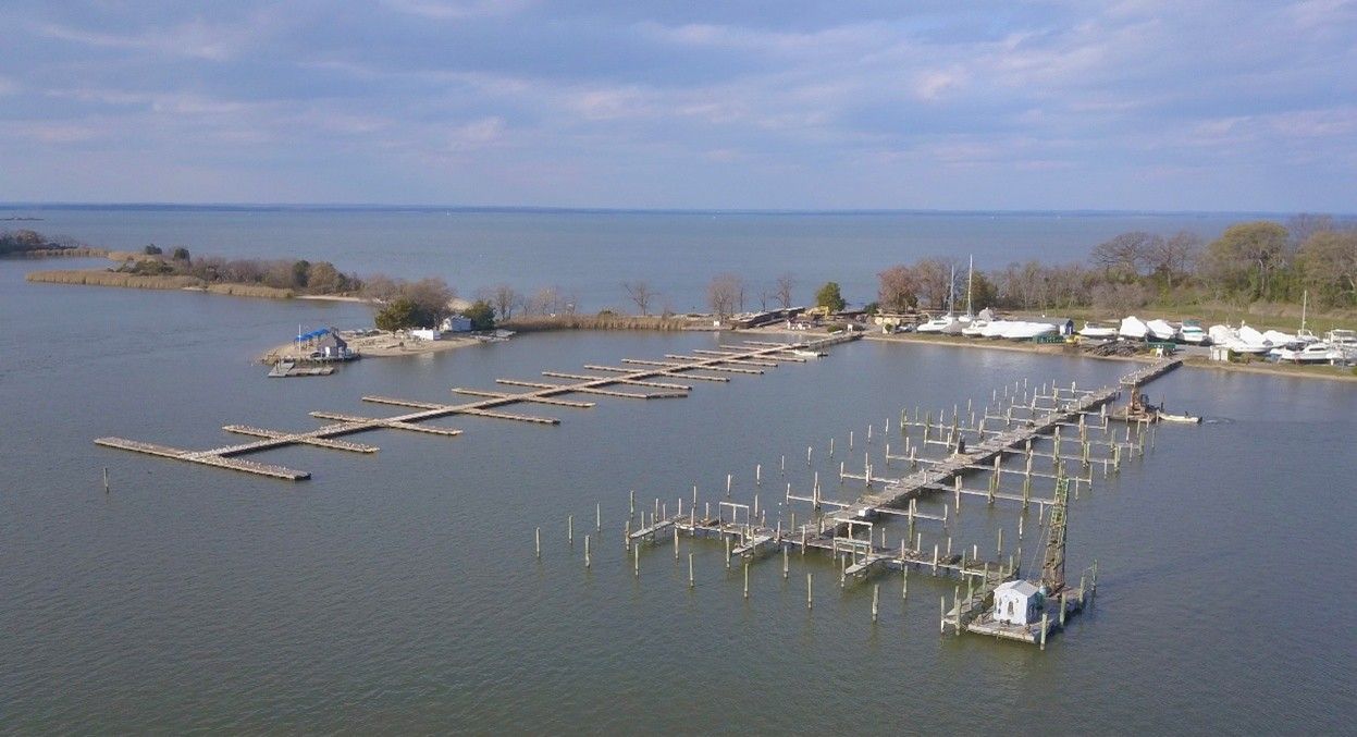 Aerial view of a marina with docks, boats, and a small island in the background, set on a body of water under a blue sky. Aerial view of a marina with docks, boats, and a small island in the background, set on a body of water under a blue sky.