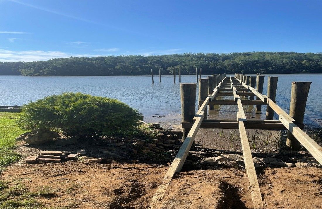 A pier under construction extends into a calm body of water; trees line the opposite shore, blue sky overhead. A pier under construction extends into a calm body of water; trees line the opposite shore, blue sky overhead.