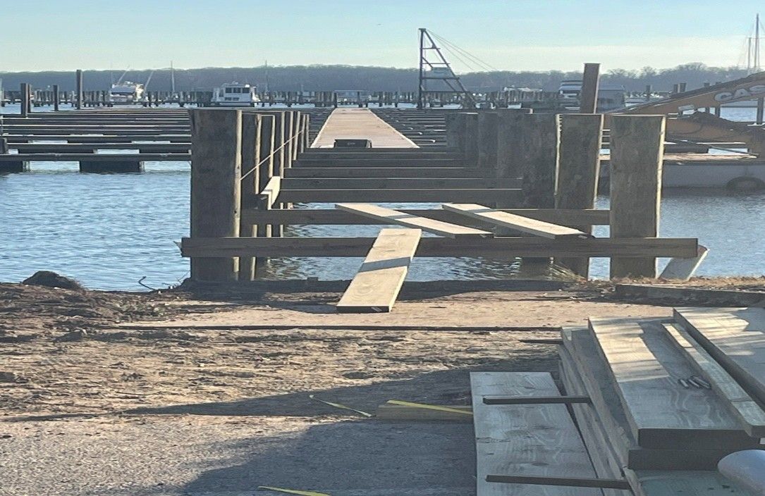 A pier under construction extends into water; wooden pilings and beams are visible. A pier under construction extends into water; wooden pilings and beams are visible.