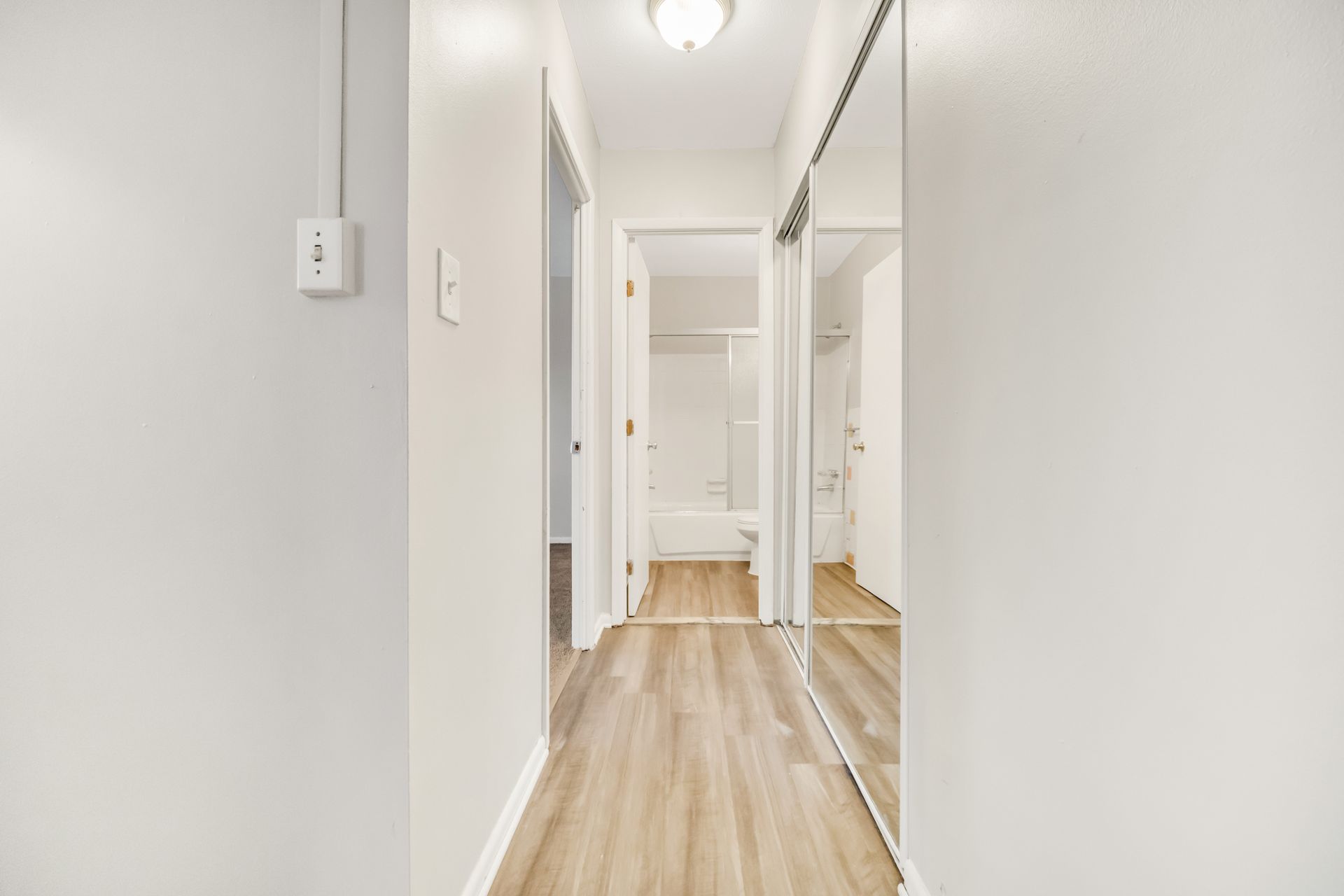 A hallway with a large mirror on the wall leading to a bathroom.