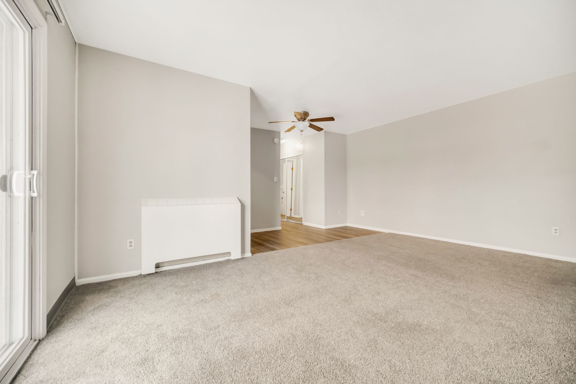 An empty living room with a ceiling fan and sliding glass doors.