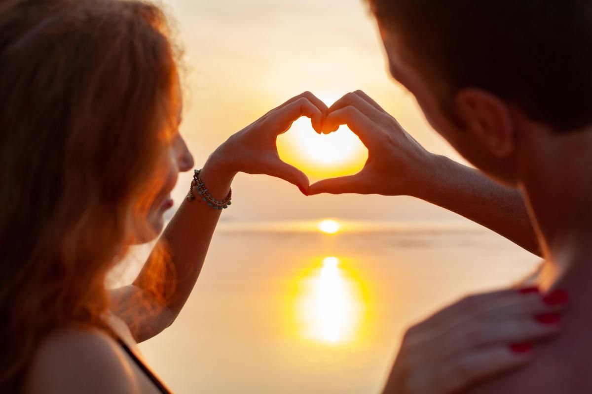 Imagem de um casal fazendo coração no pôr do sol, ilustrando uma viagem de Lua de Mel em Morro de Sã