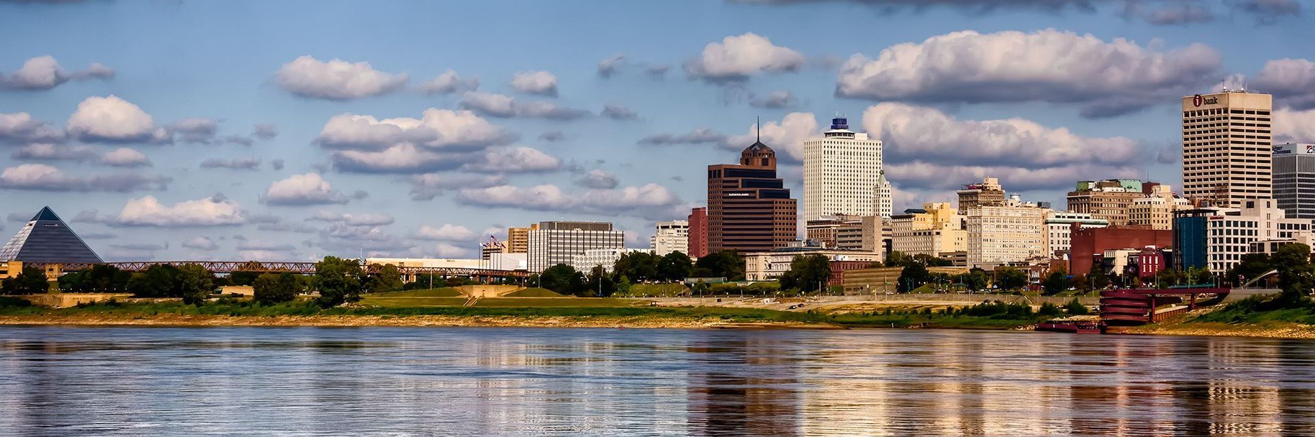 A city skyline with a lake in the foreground and a pyramid in the background.