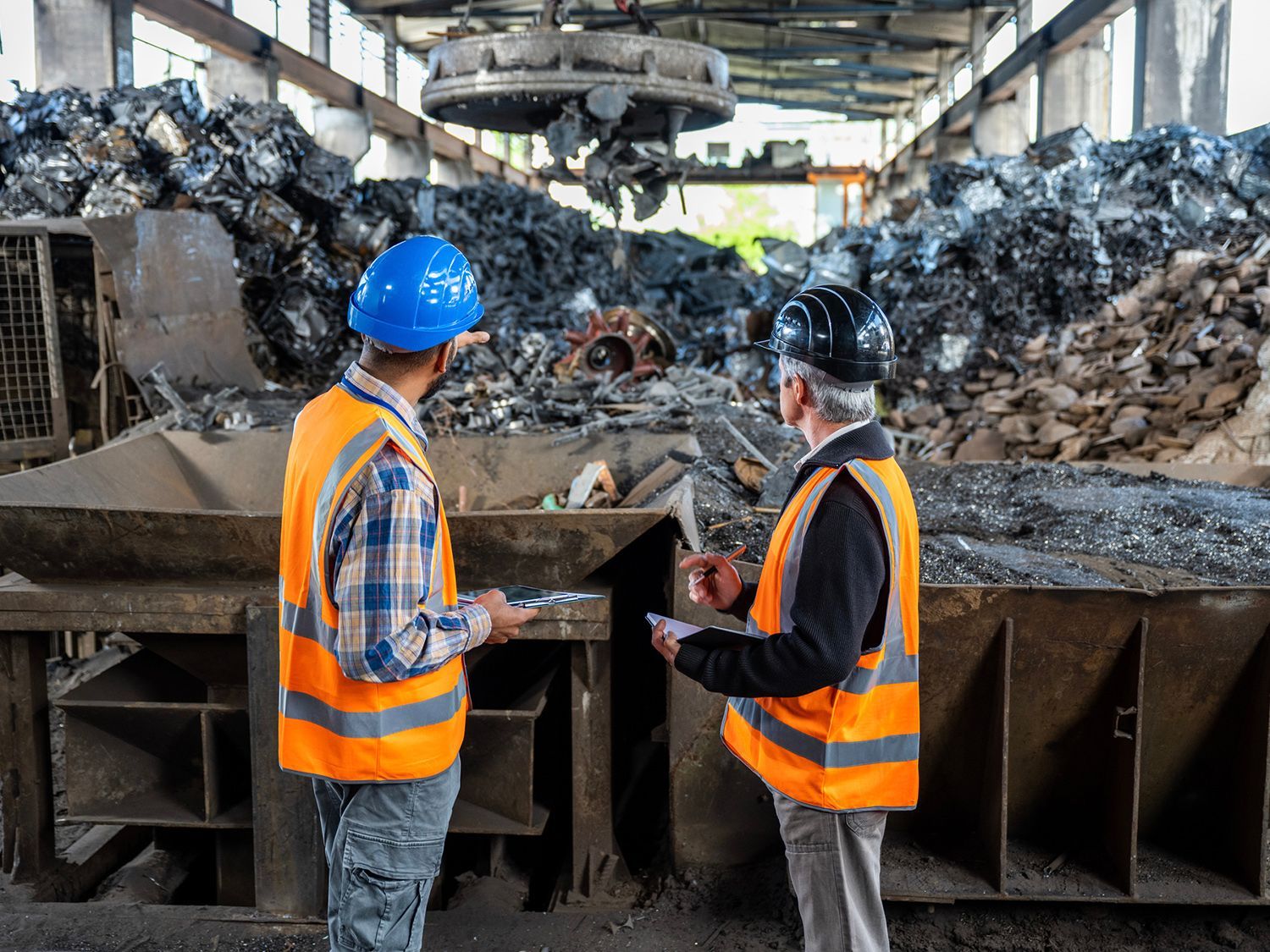 Two men are standing in front of a pile of coal in a factory.