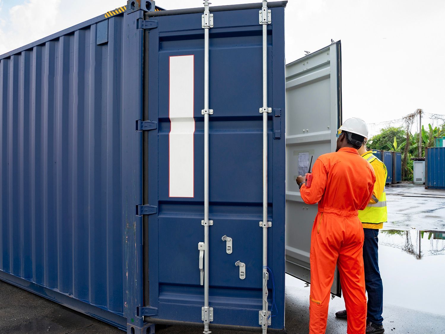 Two men are standing next to a blue shipping container.