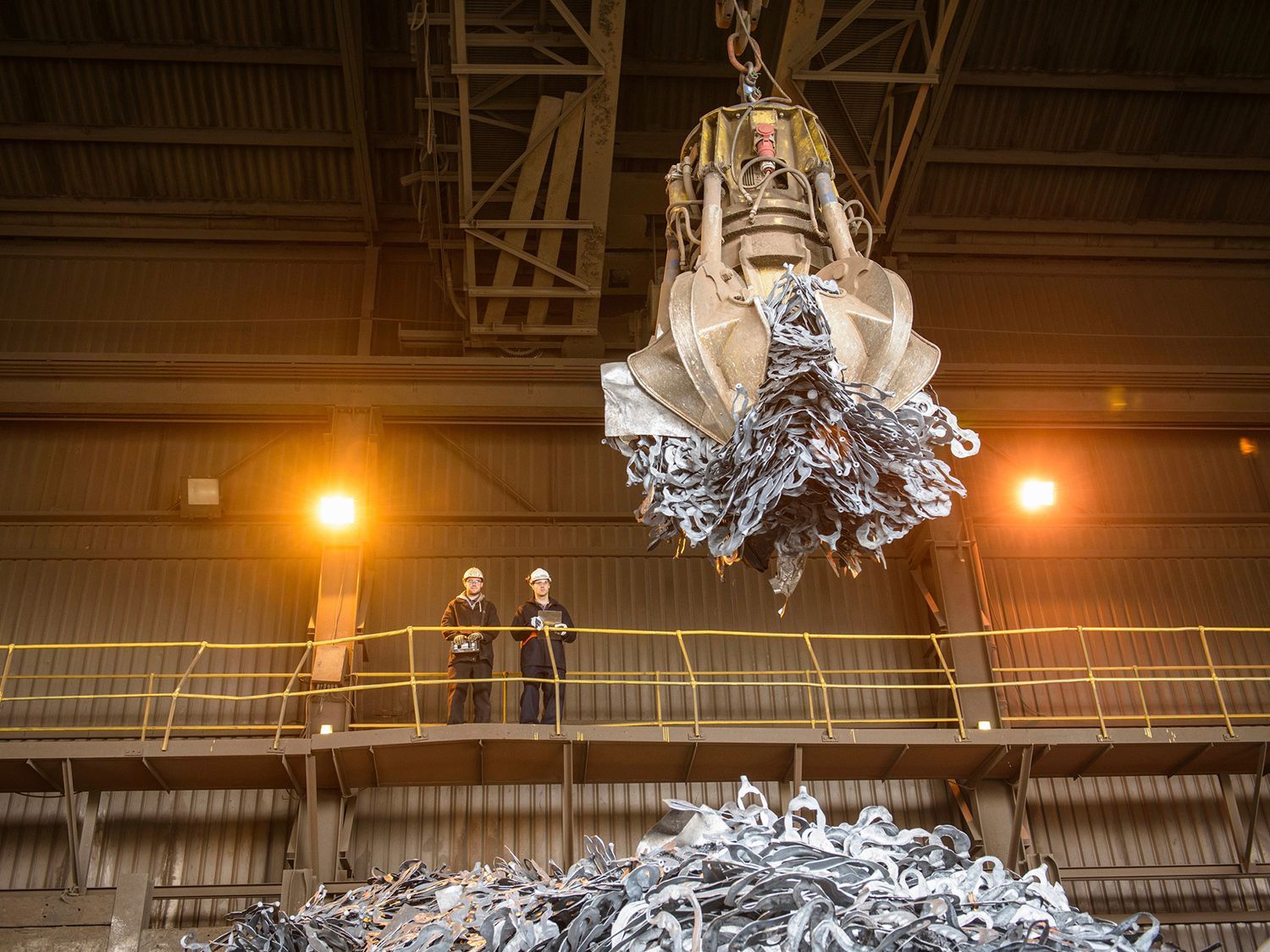 A crane is lifting a pile of metal in a factory.
