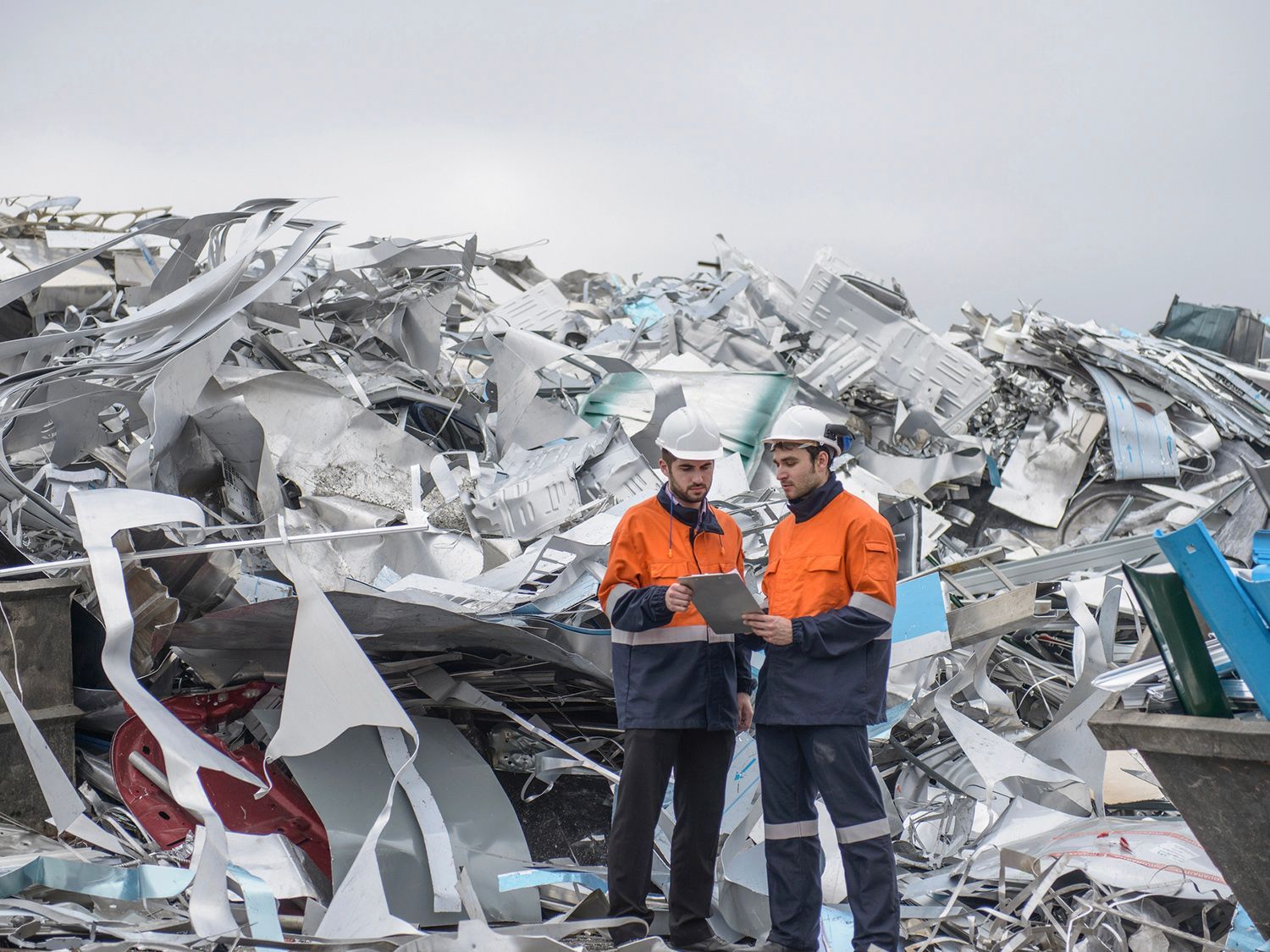 Two men are standing in front of a pile of scrap metal.