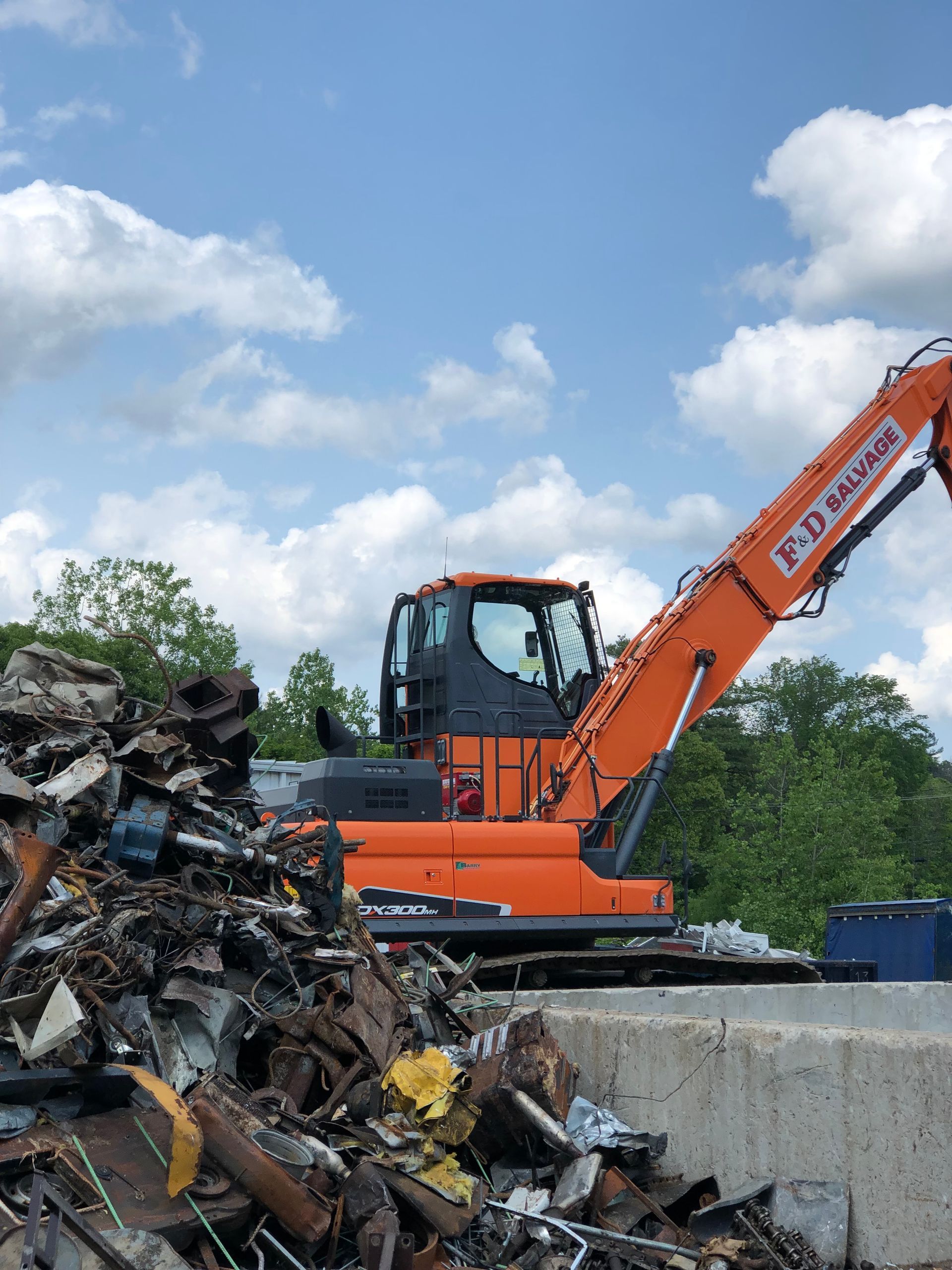 A large orange excavator is sitting on top of a pile of scrap metal.