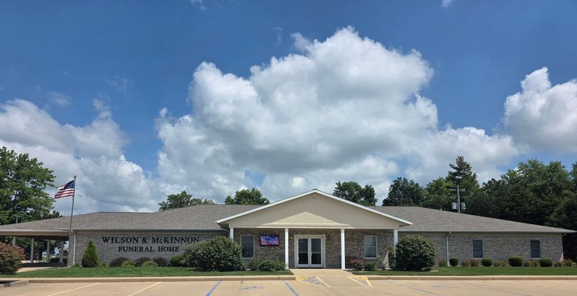 Front view of a low stone civic building with a central entrance and American flag under a blue sky