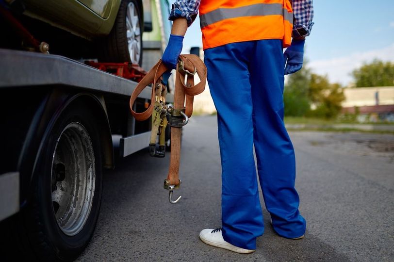 A man is standing next to a tow truck carrying a car.