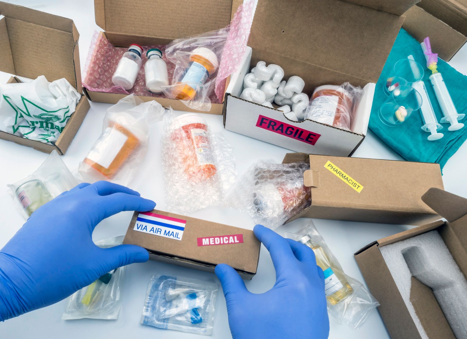 A person wearing blue gloves is packing a box of medical supplies.