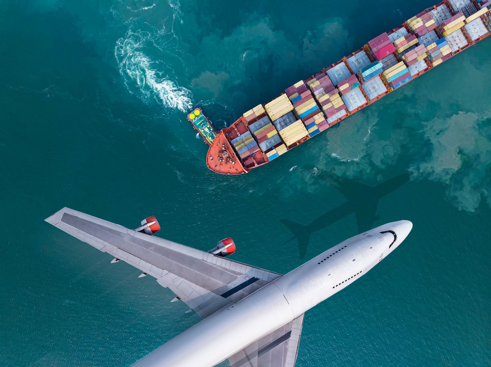 An aerial view of a plane and a cargo ship in the ocean.