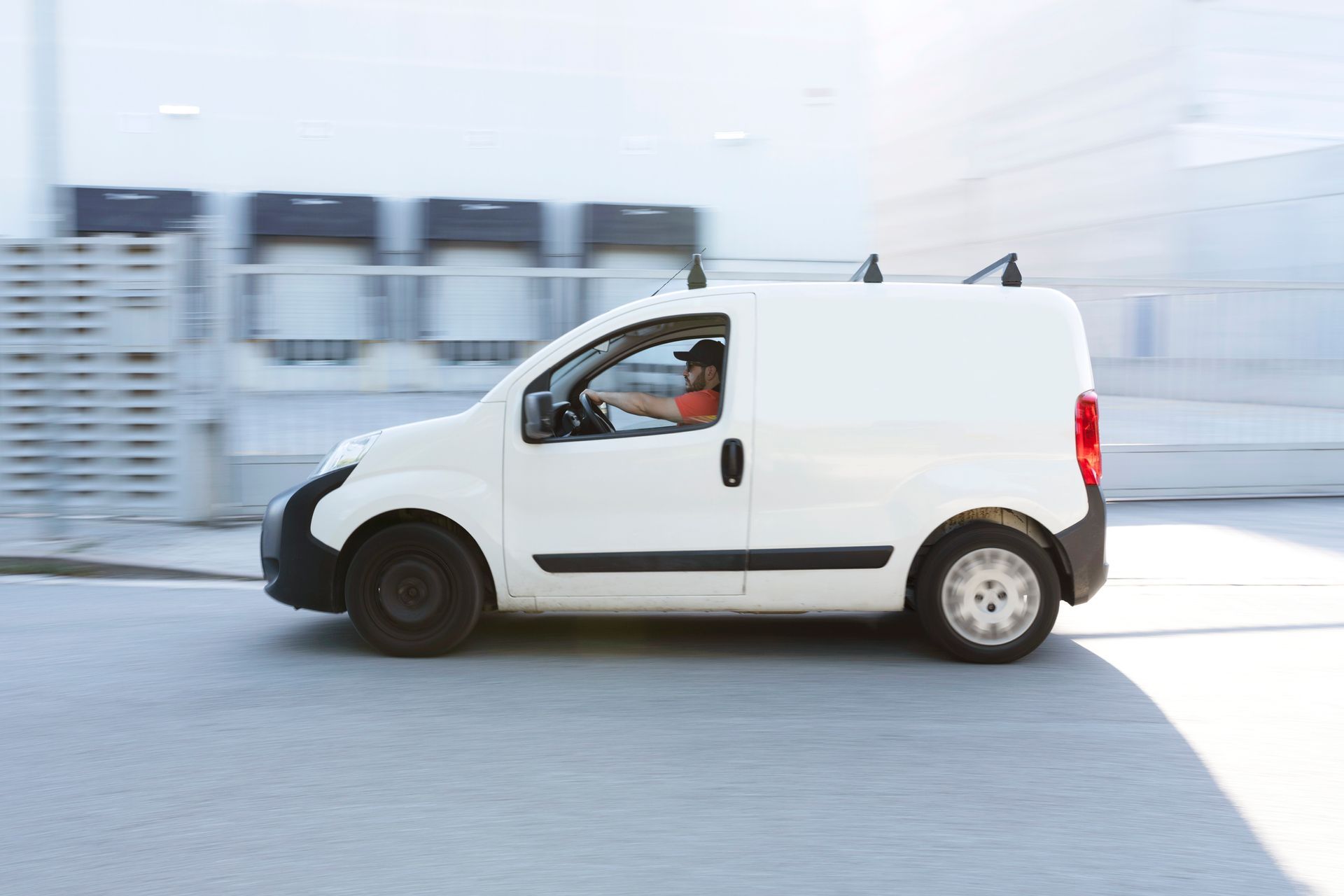A white delivery van is driving down a street in front of a warehouse.