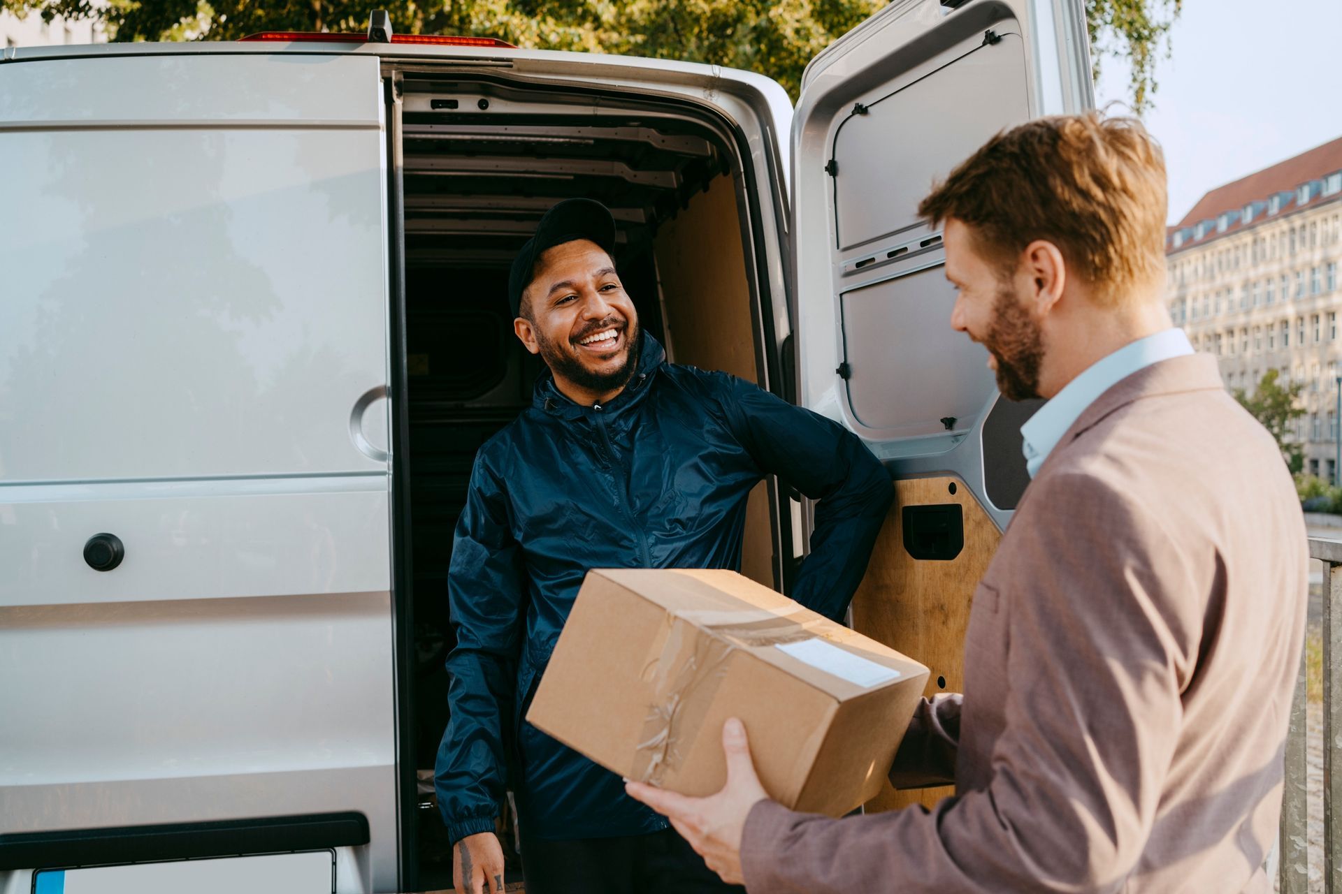 A man is giving a box to another man in front of a van.