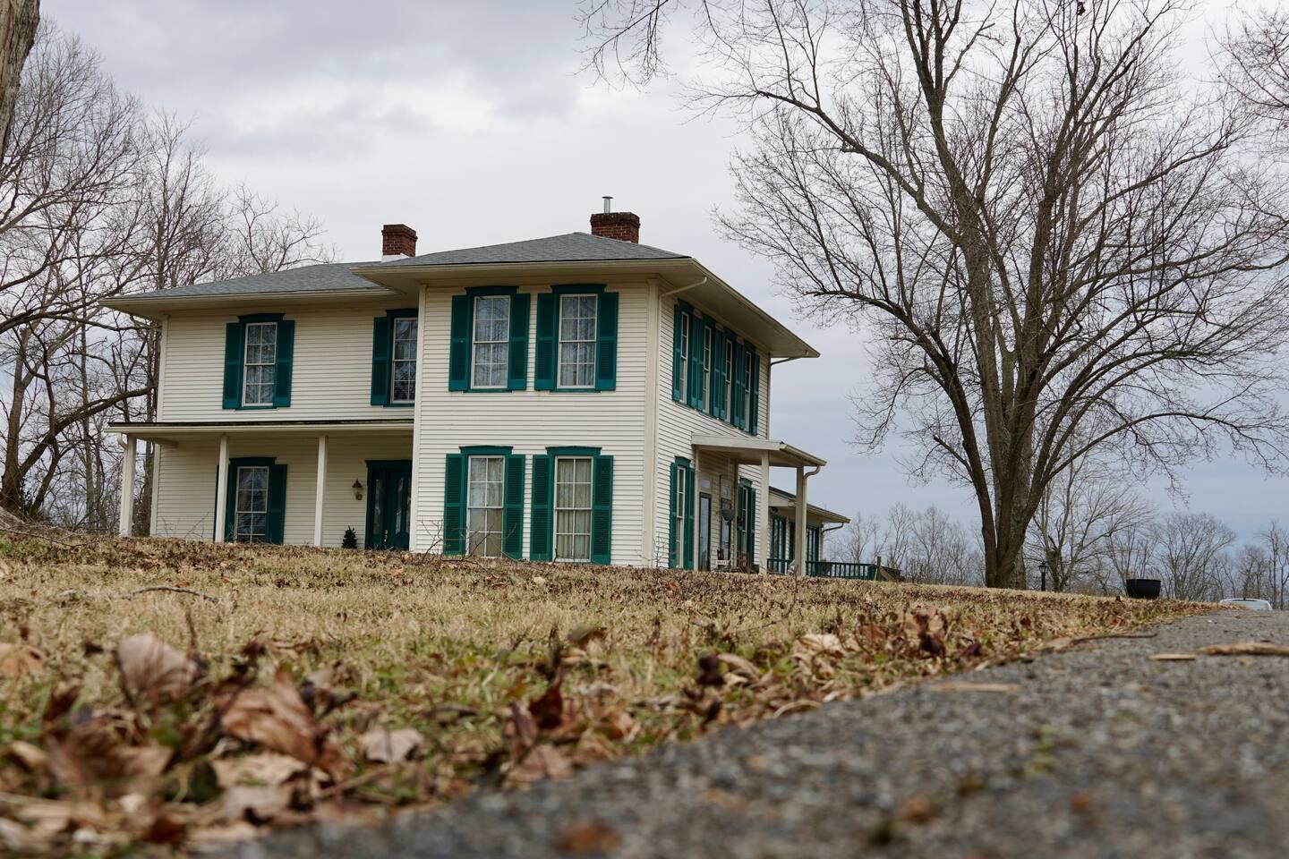 A white house with green shutters is sitting on top of a grassy hill.