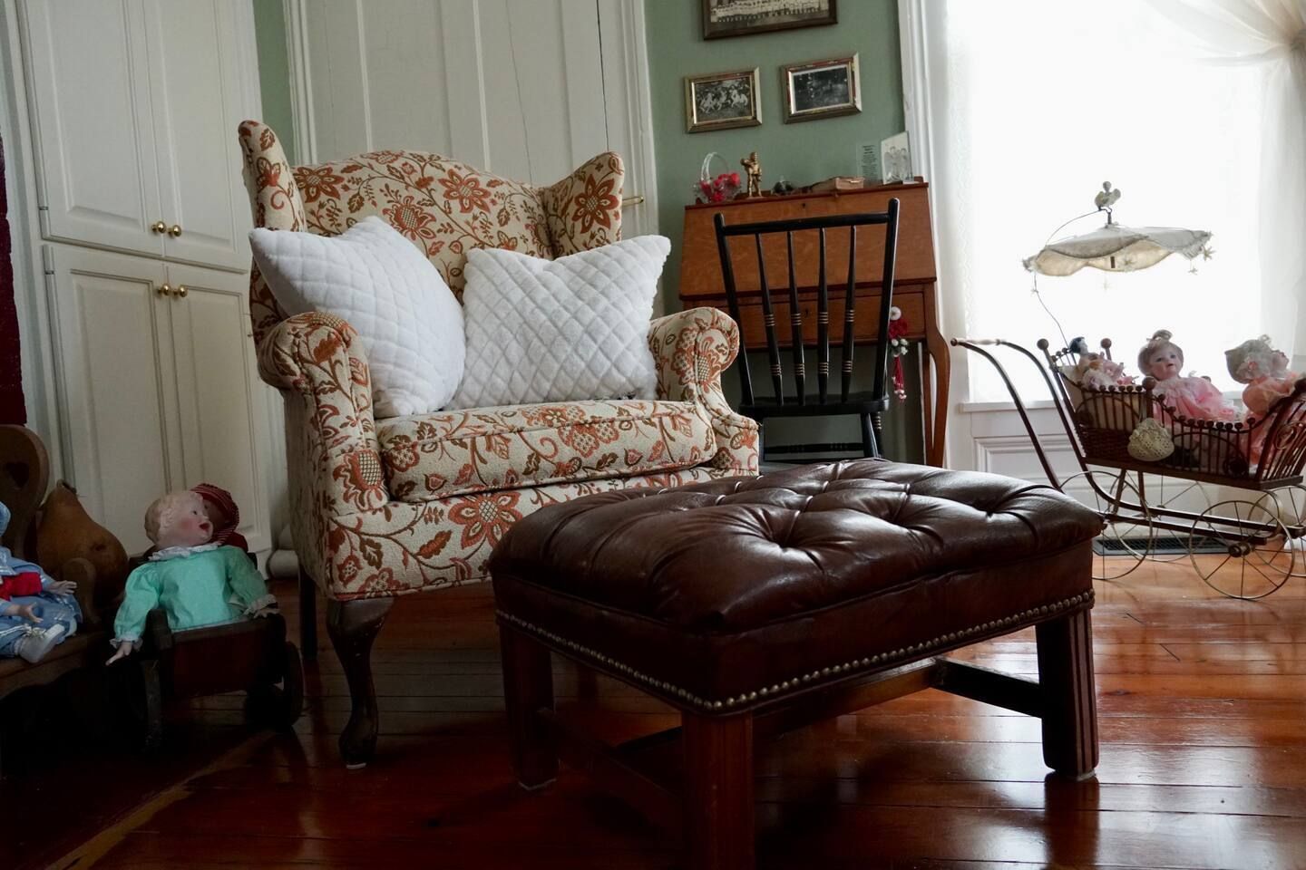 A living room with a chair , ottoman , and crib.