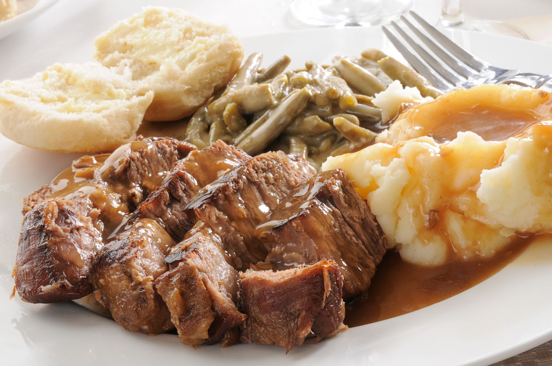 Plate of roast beef, mashed potatoes, green beans, gravy, and biscuits.