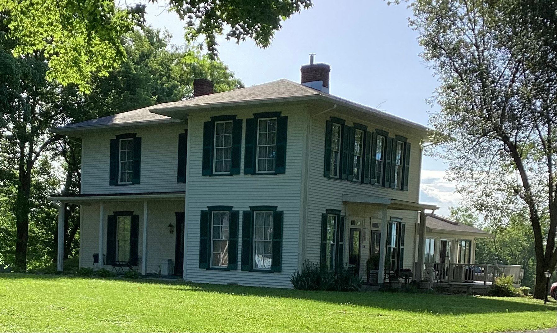 A large white house with black shutters is sitting on top of a lush green hillside.