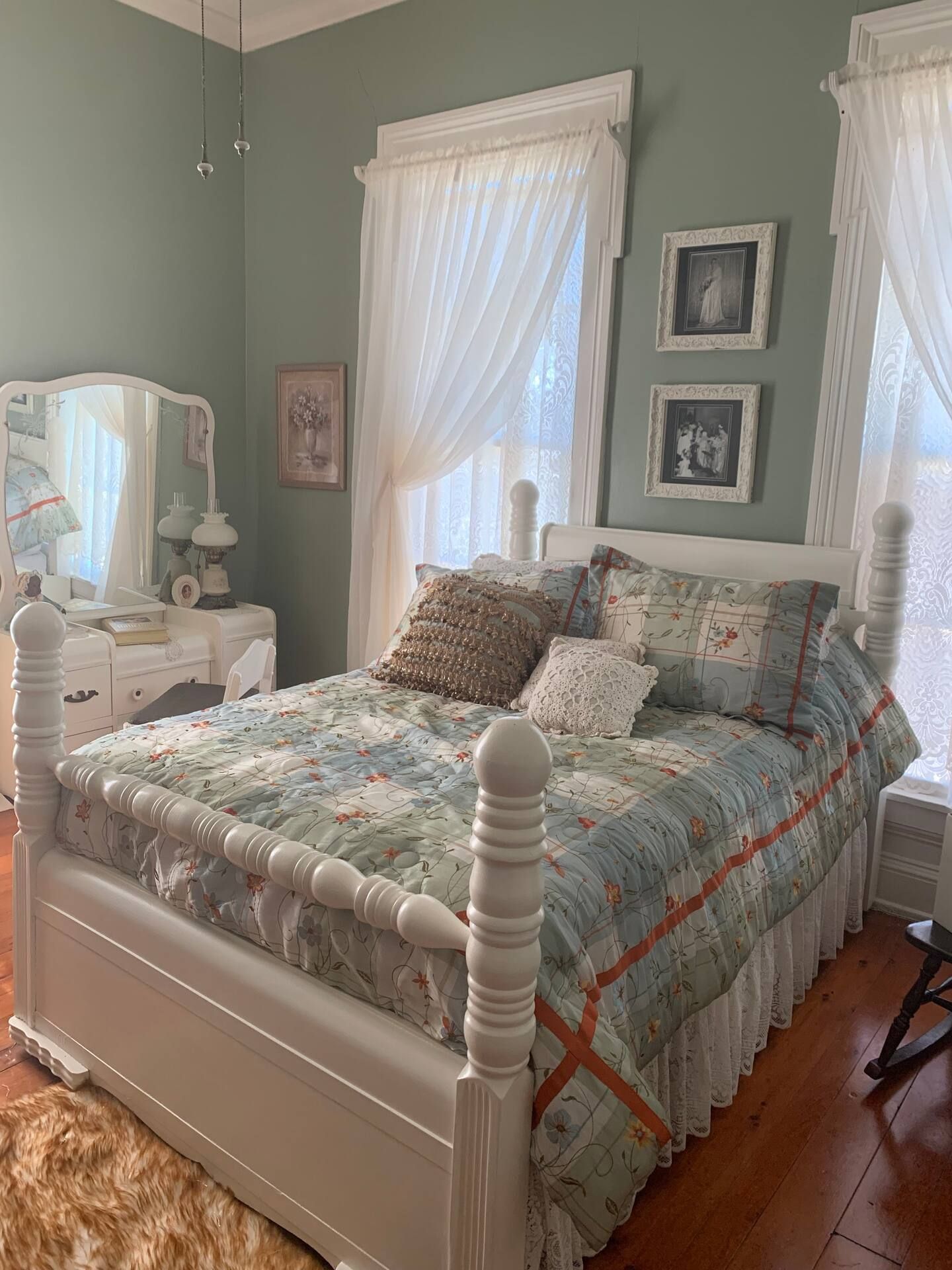 A bedroom with a bed , dresser , mirror and two windows.