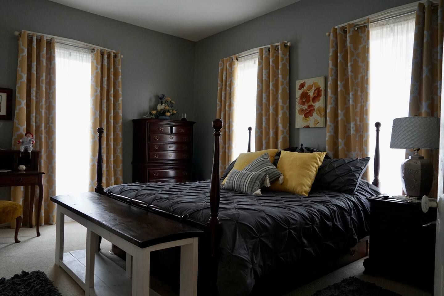 A bedroom with a bed , dresser , nightstand , and two windows.