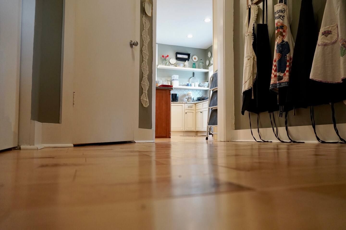 A hallway with a wooden floor and a kitchen in the background.