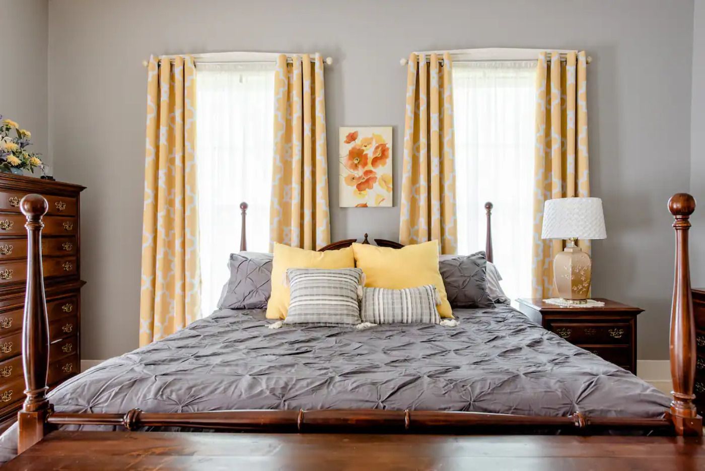 A bedroom with a bed , dresser , nightstand and two windows.