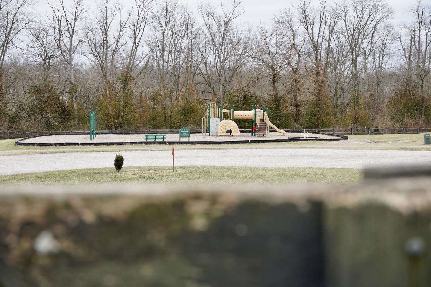 A playground is visible through a wooden fence in a park.