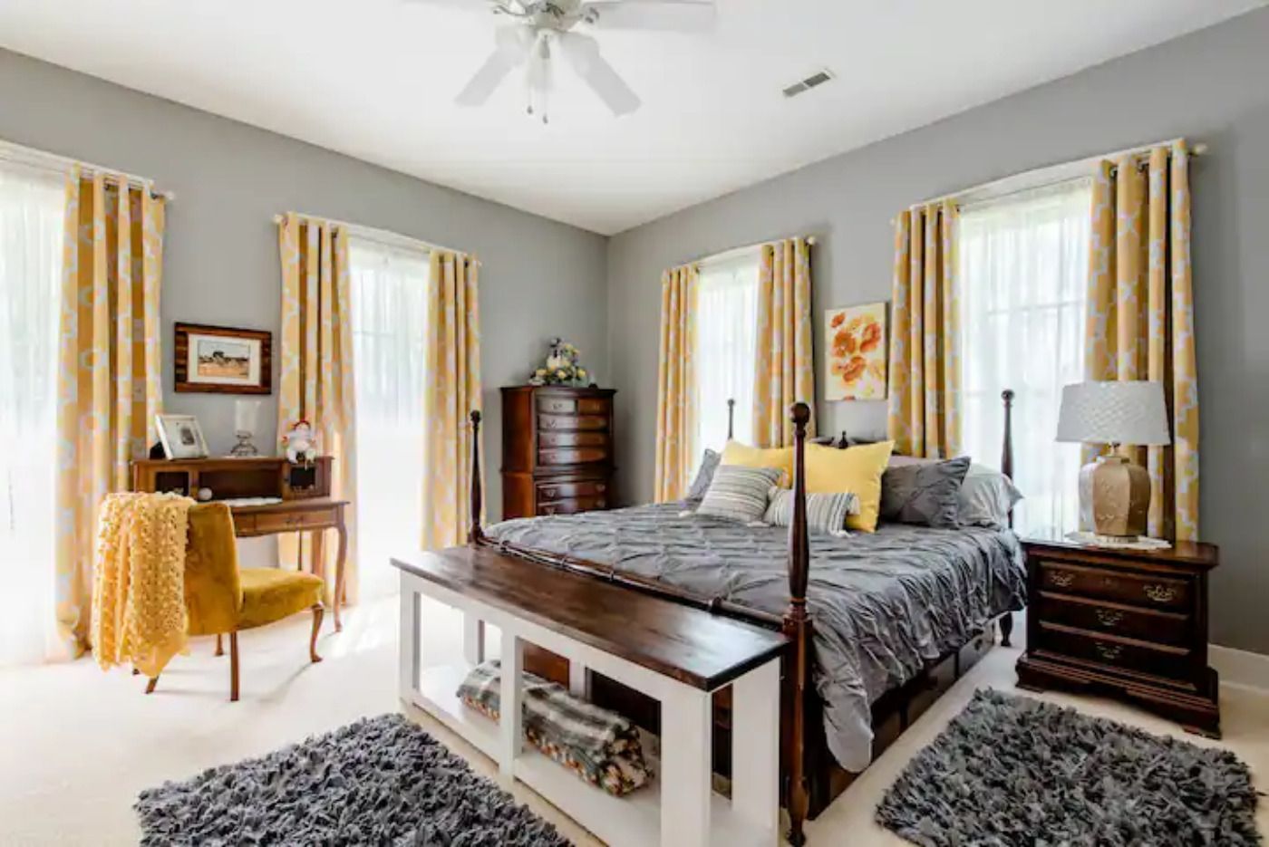 A bedroom with a bed , desk , nightstand , rug and ceiling fan.