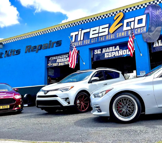 Three men in front of a tire shop sign. They are wearing uniforms, and smiling. American flag visible.