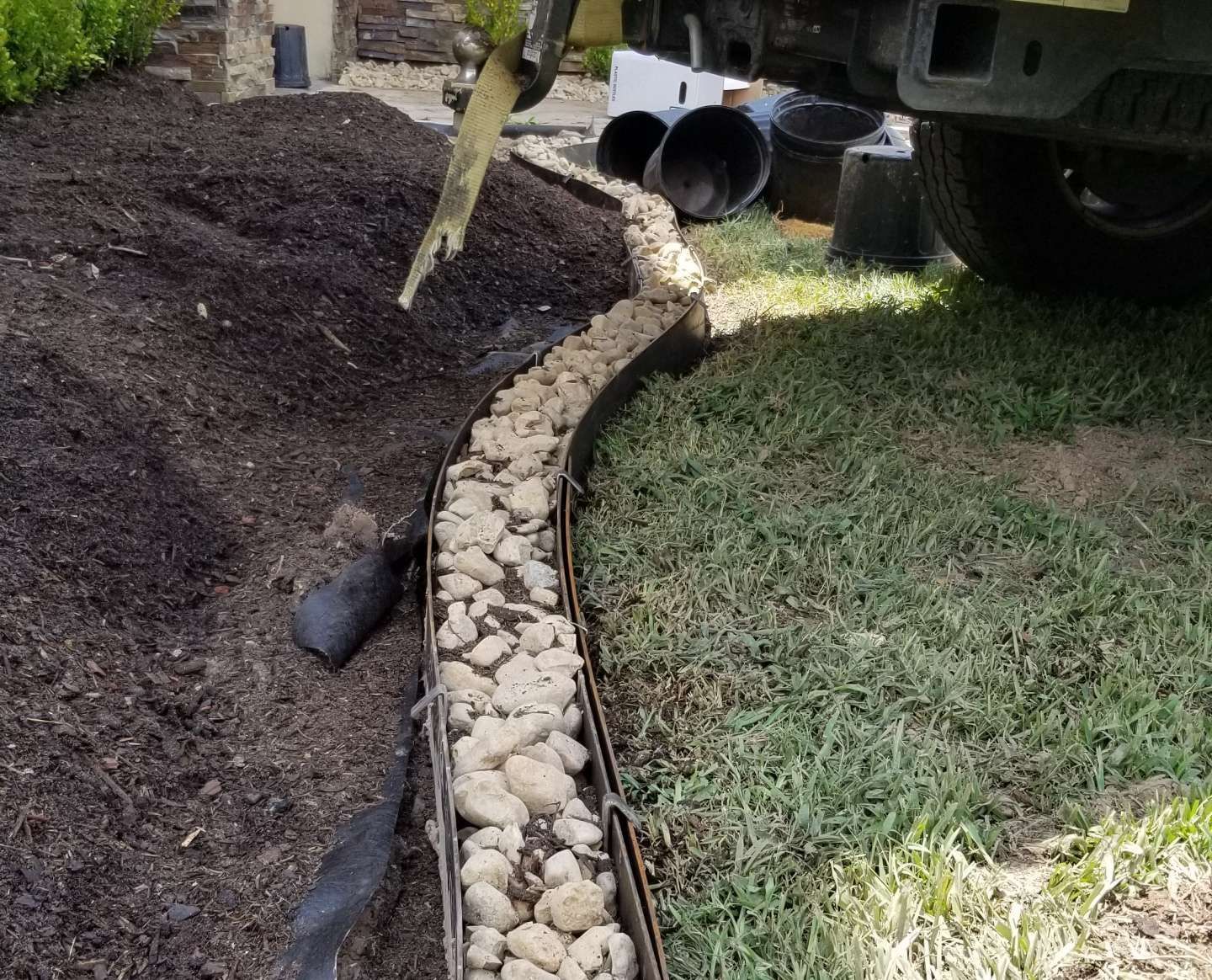 Landscaping border construction: curved metal edging with gravel separating mulch and grass.
