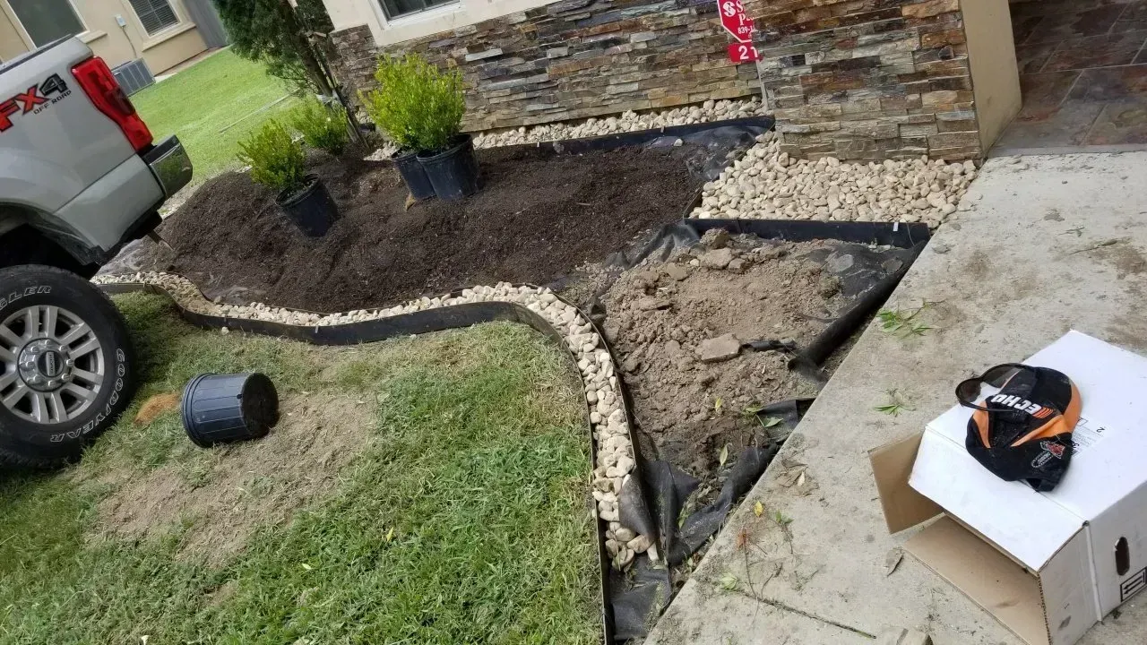 Landscaped yard with truck parked. Mulch, stones, plants, and gardening supplies are present.