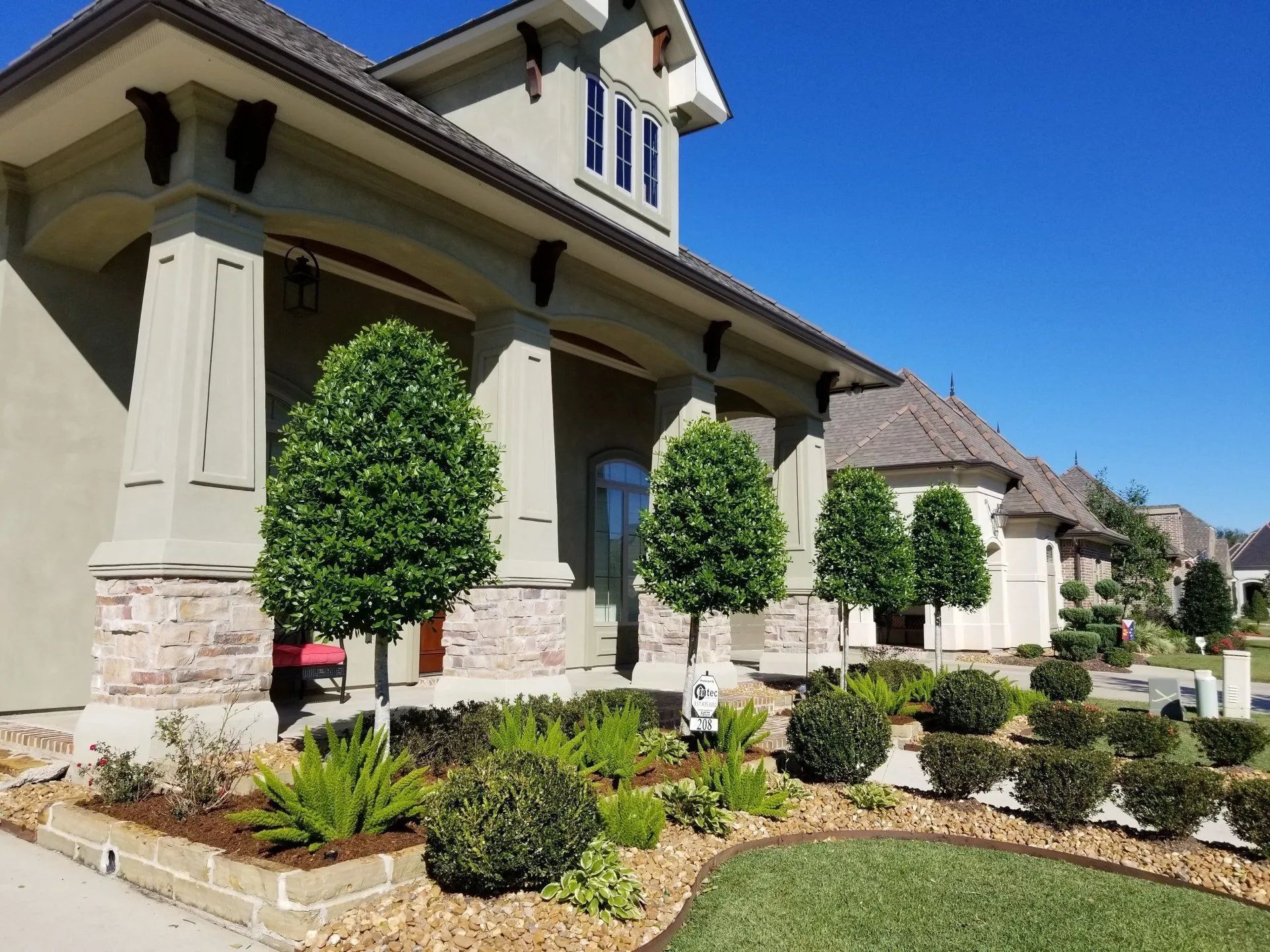 Tan house with columns and landscaped yard under a blue sky.