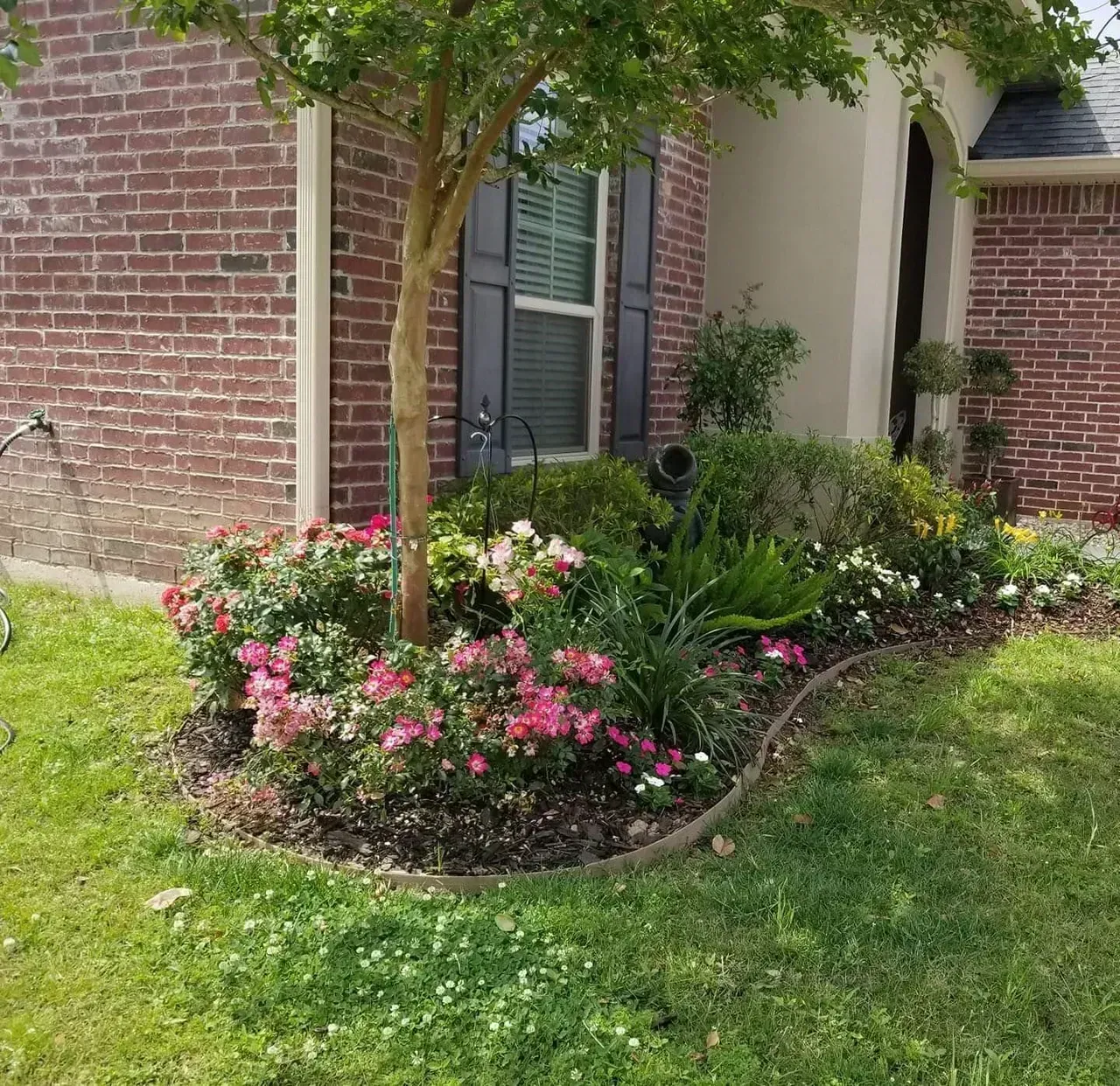 A colorful garden bed with blooming pink and white flowers sits in front of a brick house.