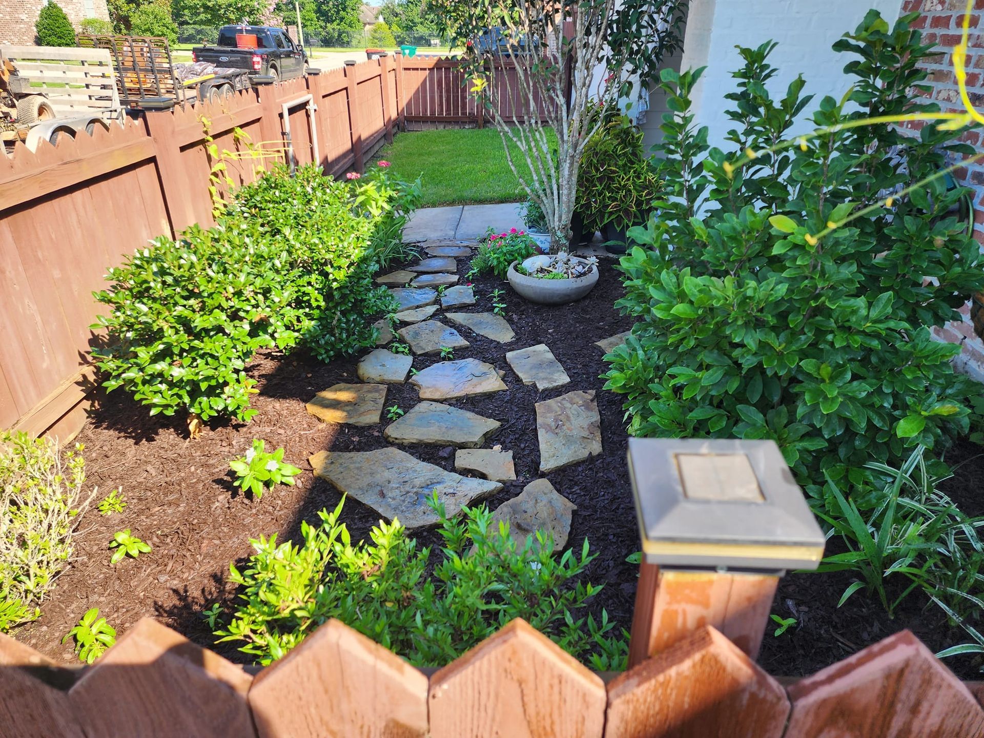 A garden path with stone steps leads to a grassy area, surrounded by bushes and a wooden fence.
