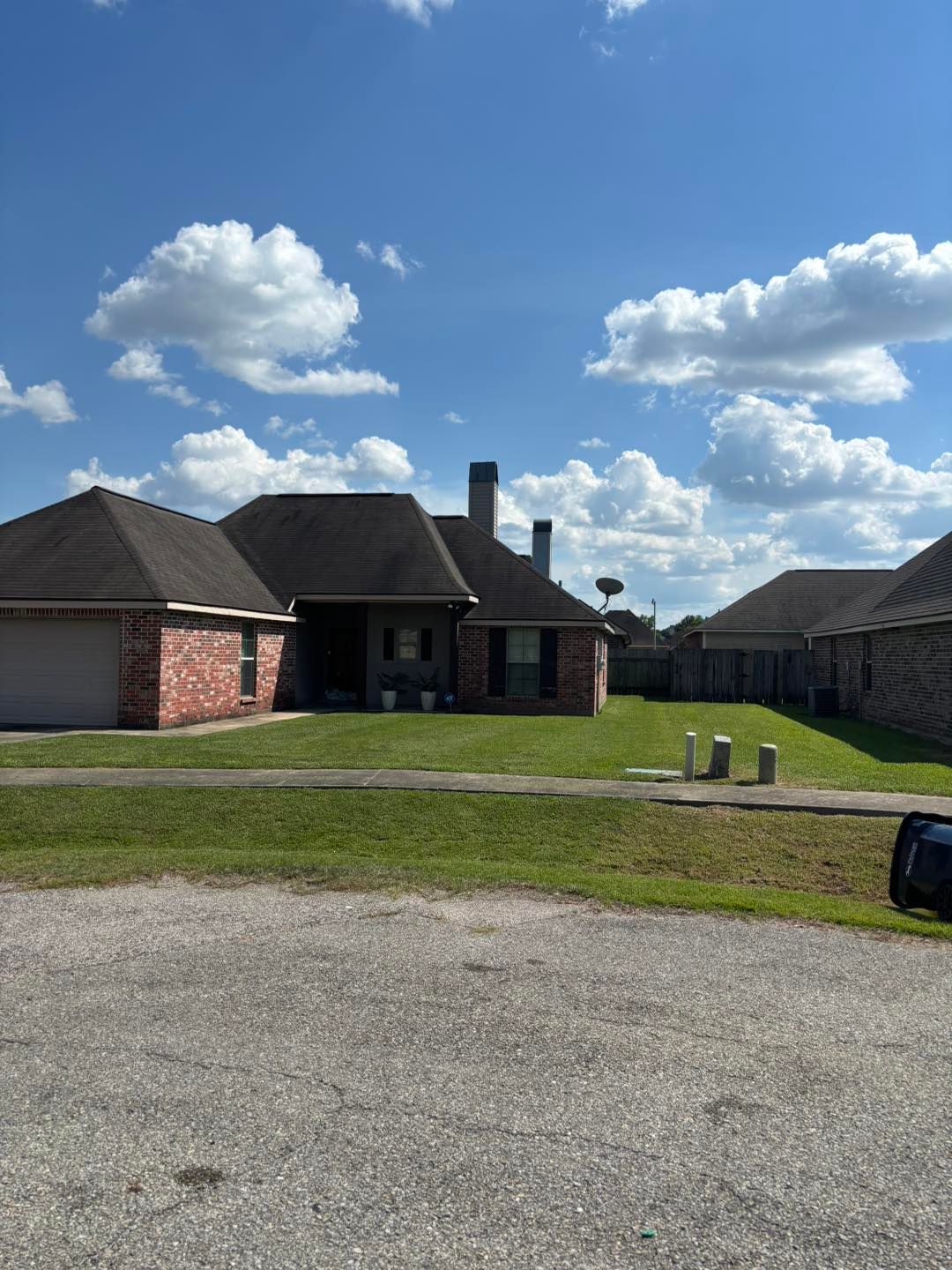 Brick house with dark roof and green lawn on a sunny day with clouds.