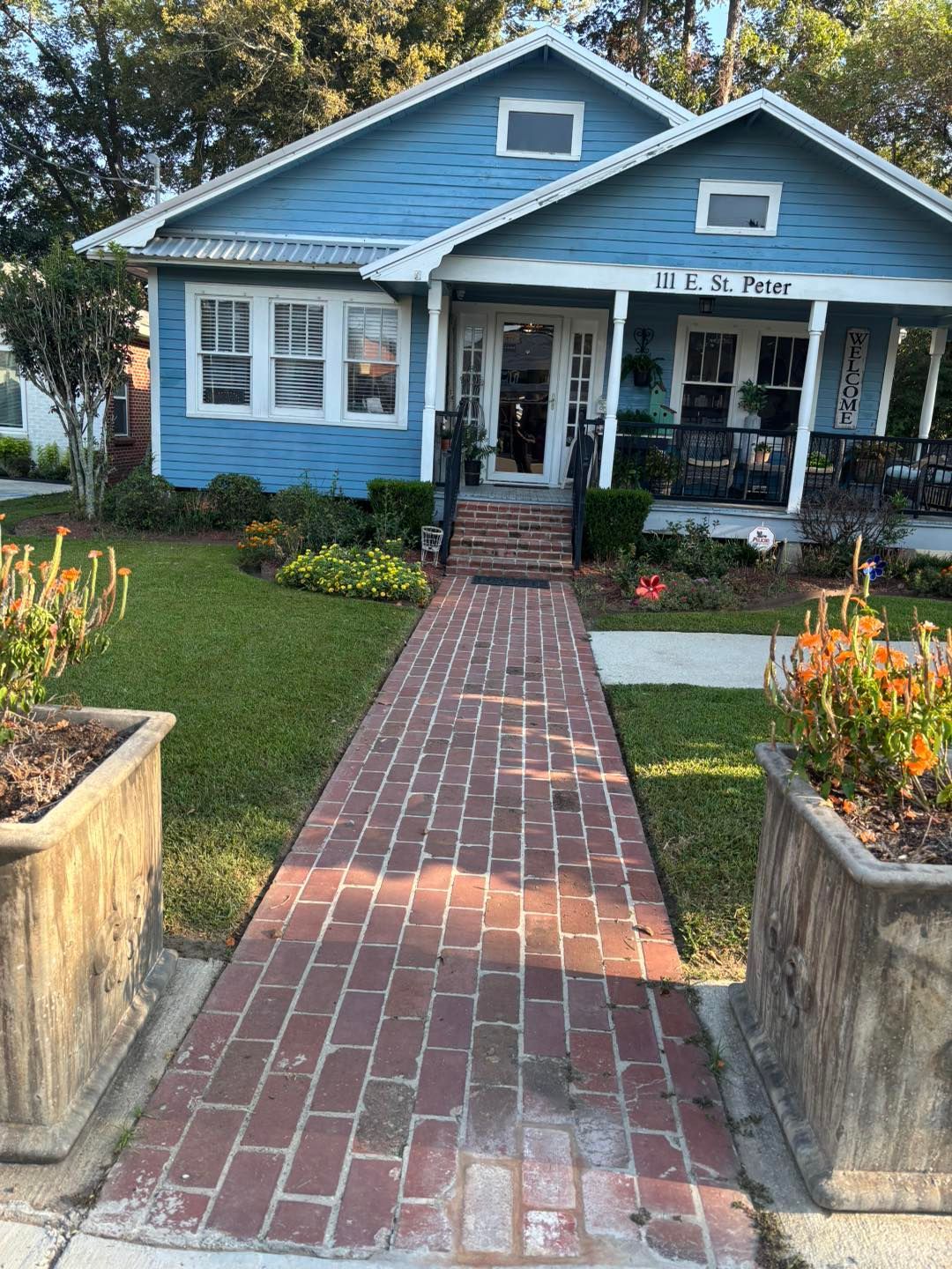 Brick walkway leading to a blue house with a porch and flowerbeds.