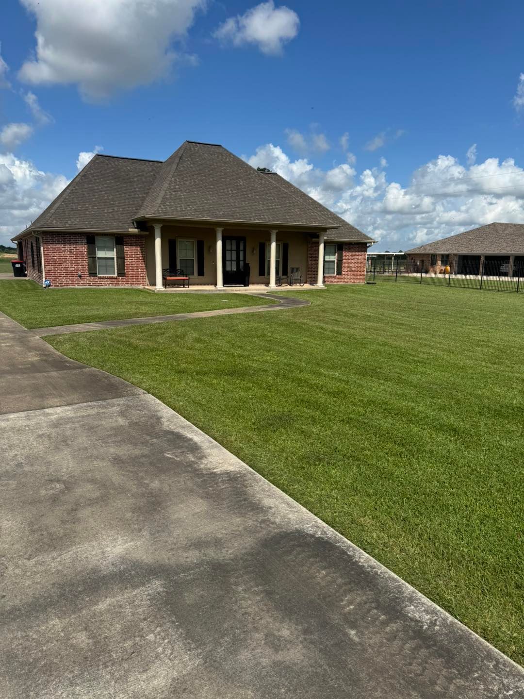 Brick house with porch and green lawn under a blue sky with clouds.