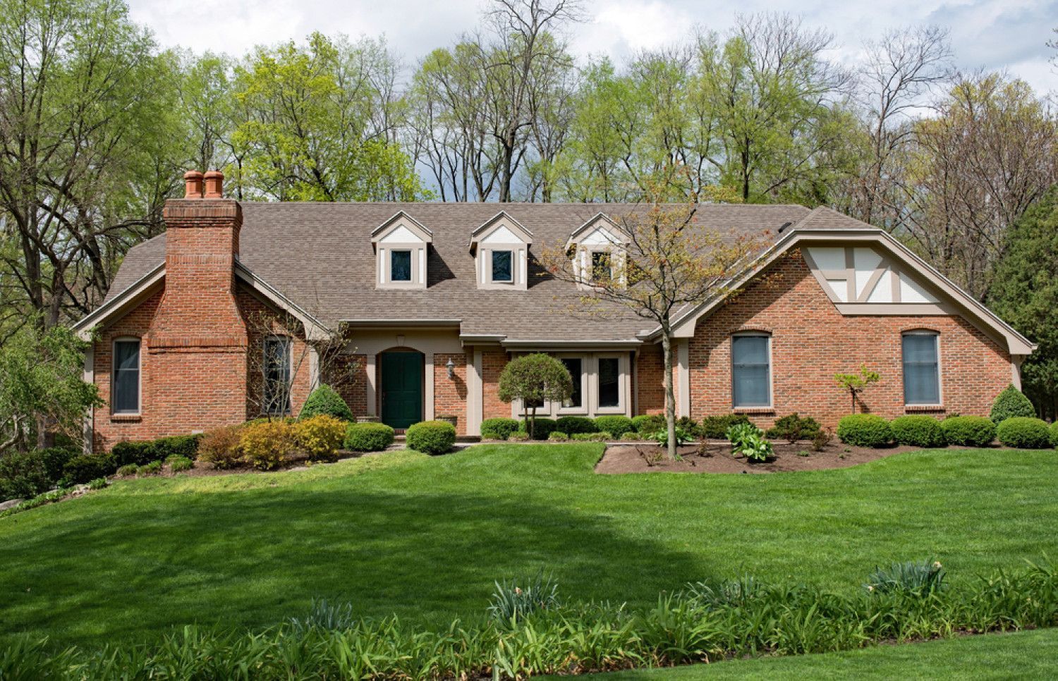 Brick house with green lawn, trees, and three dormer windows.