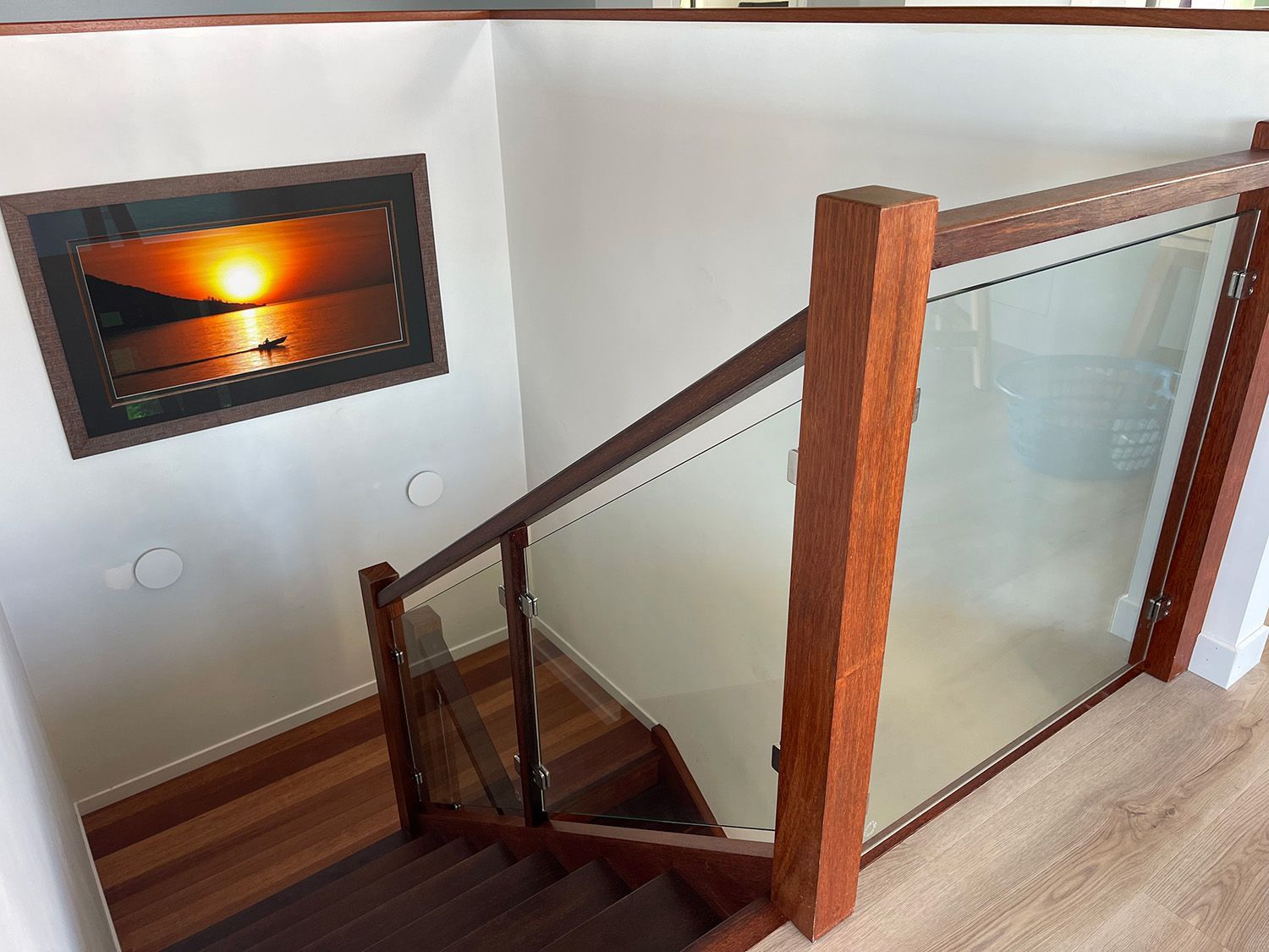 Wooden Staircase With Glass Railing And Sunset Artwork On Wall