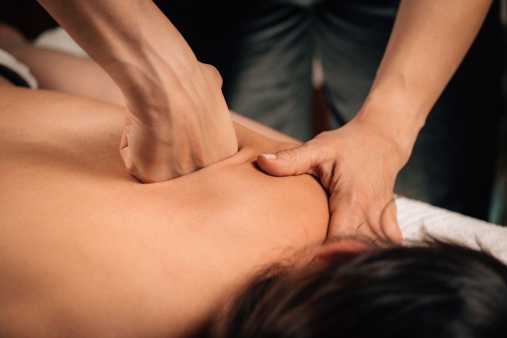 Hands giving a shoulder massage to a person lying face down on a massage table