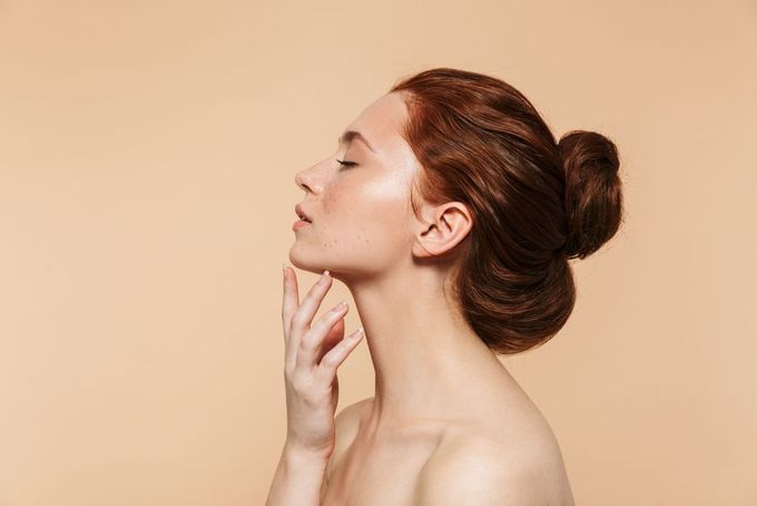 Profile of a person with hair in a bun, gently touching their chin against a beige background