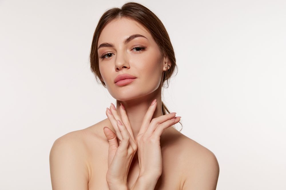Portrait of a woman against a white background, with hands gently touching her neck and a calm expression
