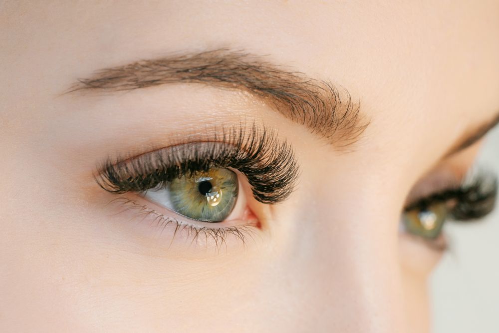 Close-up of a green eye with long lashes and shaped eyebrow on a pale face