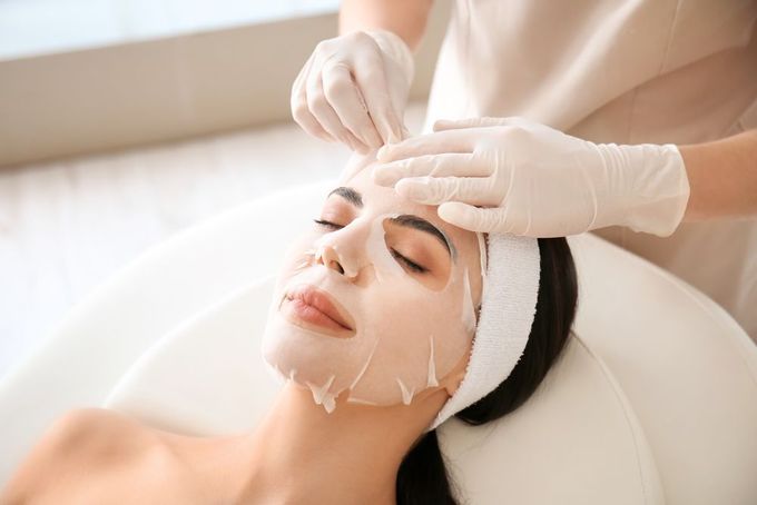 Esthetician applying a facial mask to a reclining client in a spa treatment room