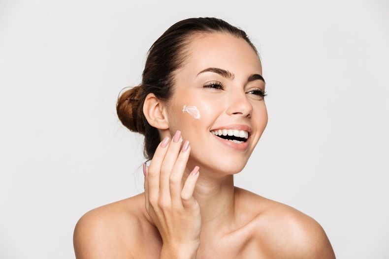 Woman applying cream to her cheek, smiling against a white background