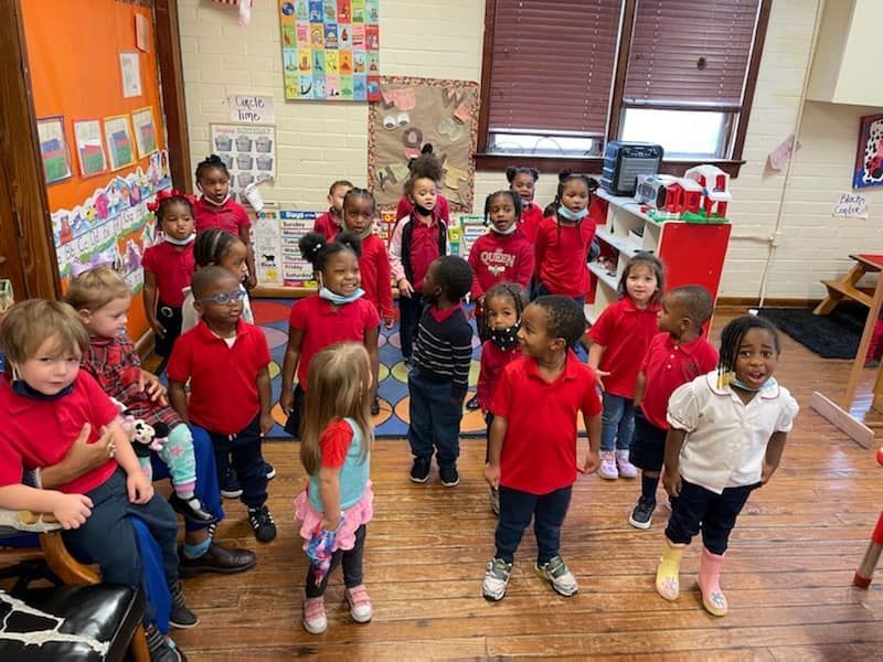 a group of children in red shirts are standing in a classroom .