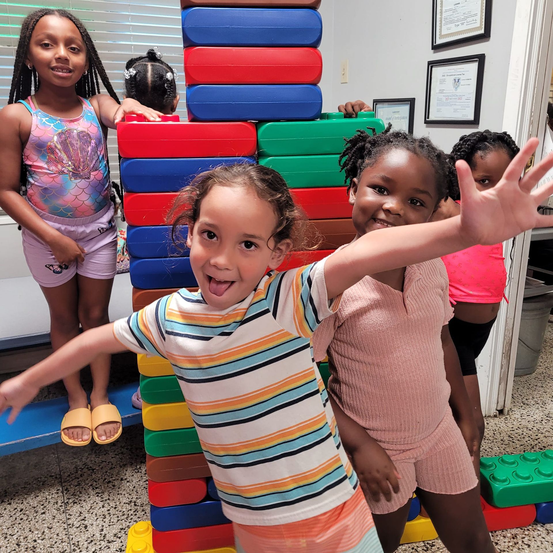 a group of young girls are standing in front of a giant stack of lego blocks .