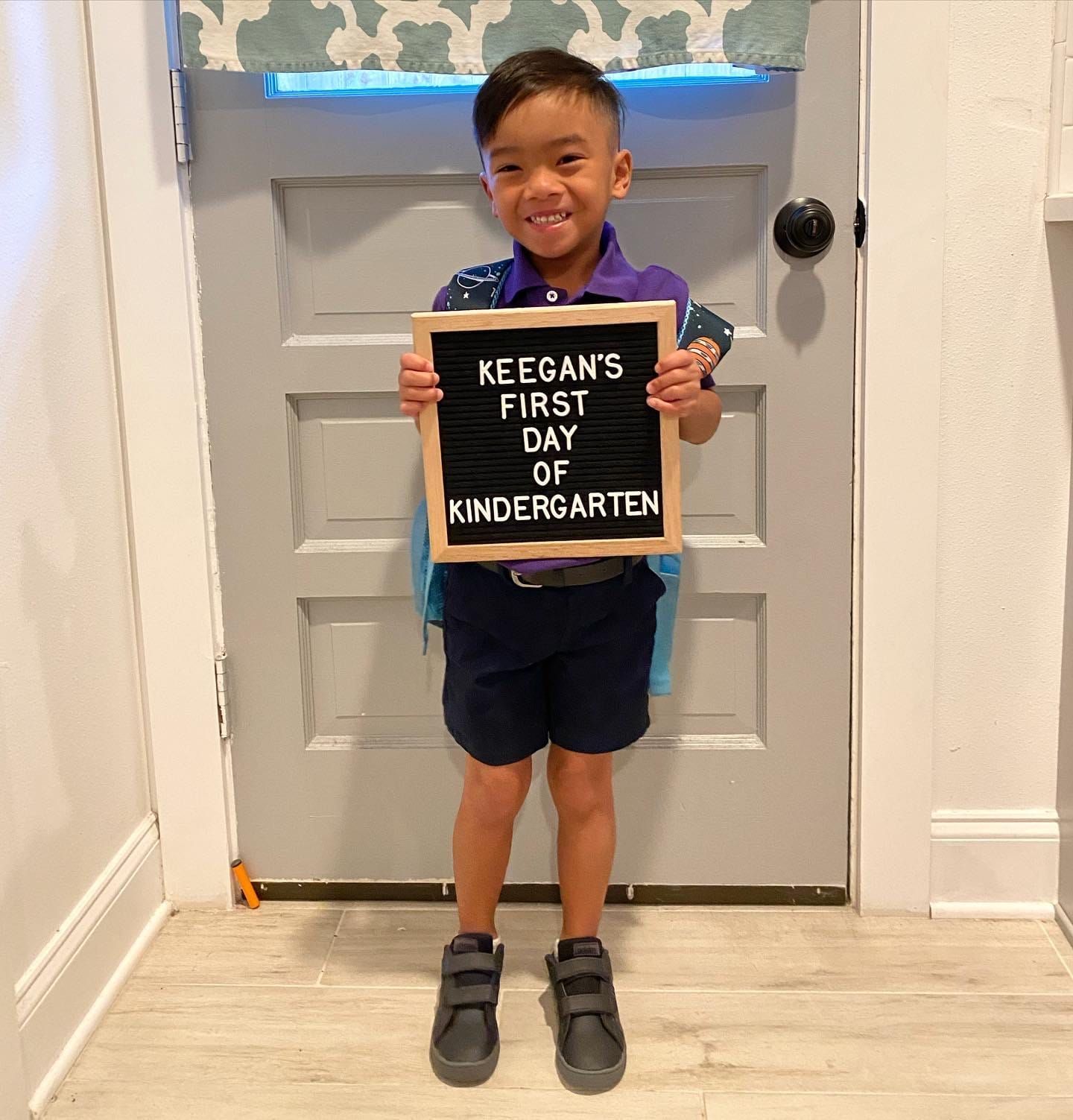 a young boy is holding a sign that says keegan 's first day of kindergarten