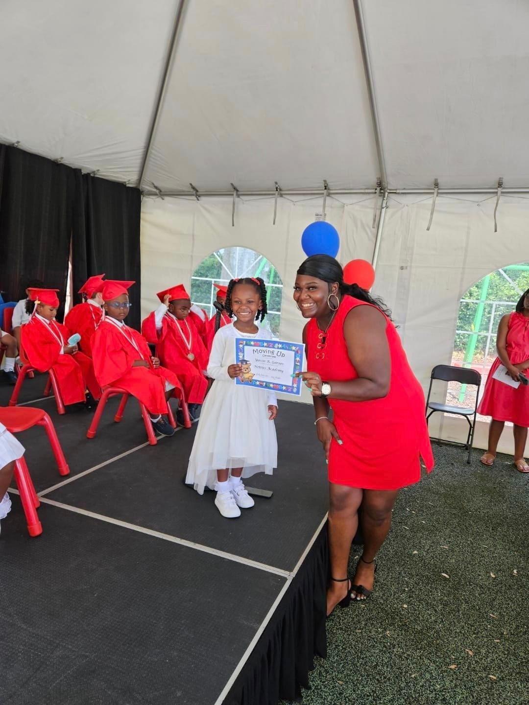 a woman in a red dress is holding a certificate for a little girl